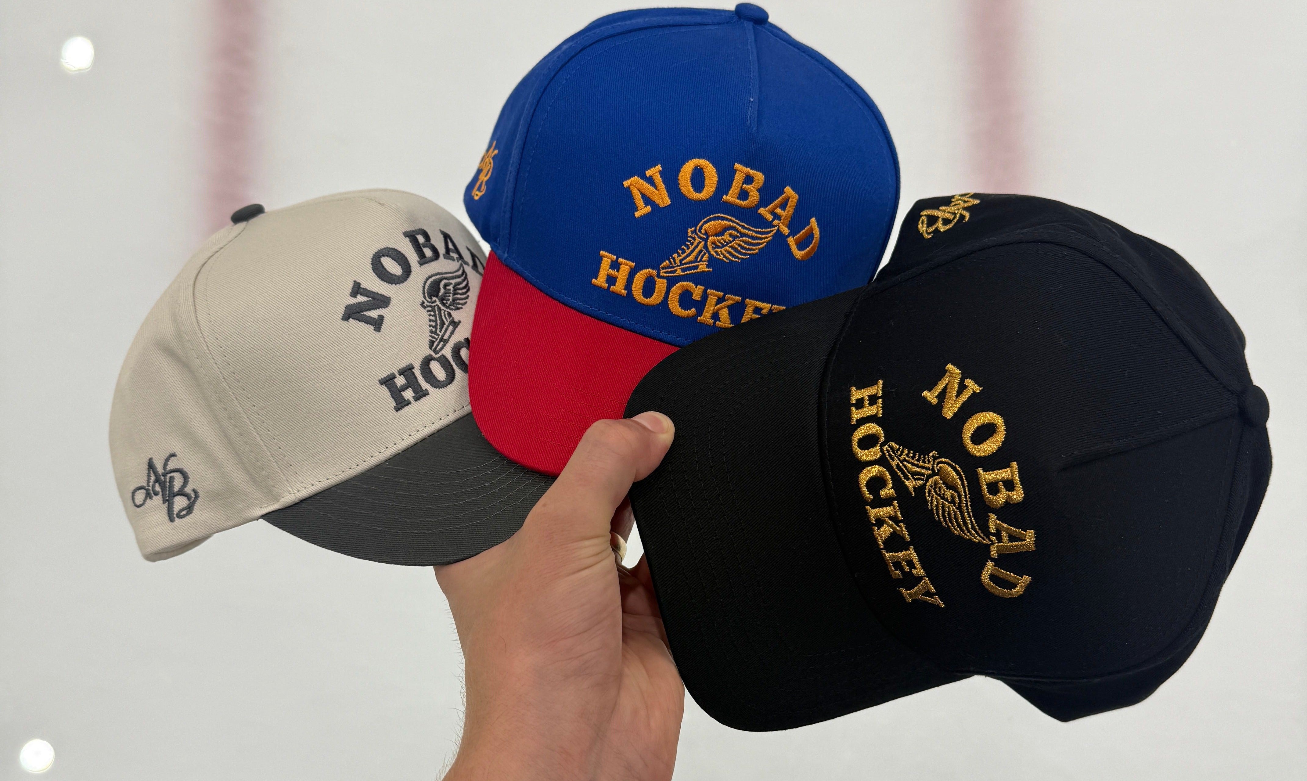 Three NOBAD vintage hockey hats held up at the rink